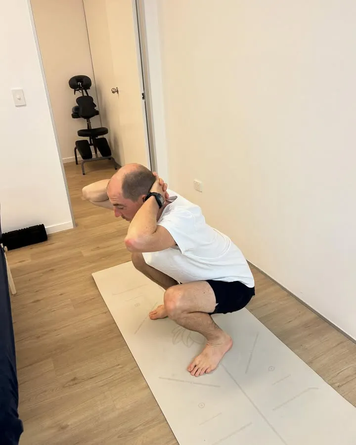 Man squatting on yoga mat indoors.